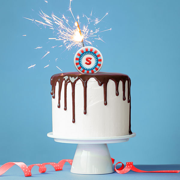 Birthday cake with white icing and chocolate drizzle and a Shorelines Casinos sparkler on a cake.